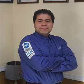 Man in blue shirt with arms crossed, standing near a lamp. Has an I-CAR patch on the sleeve.