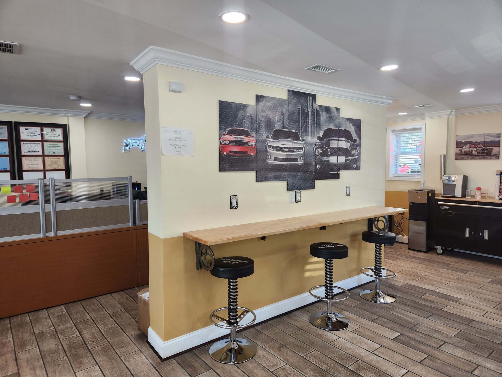 Interior of a shop with a bar area, stools, and car art on the wall.