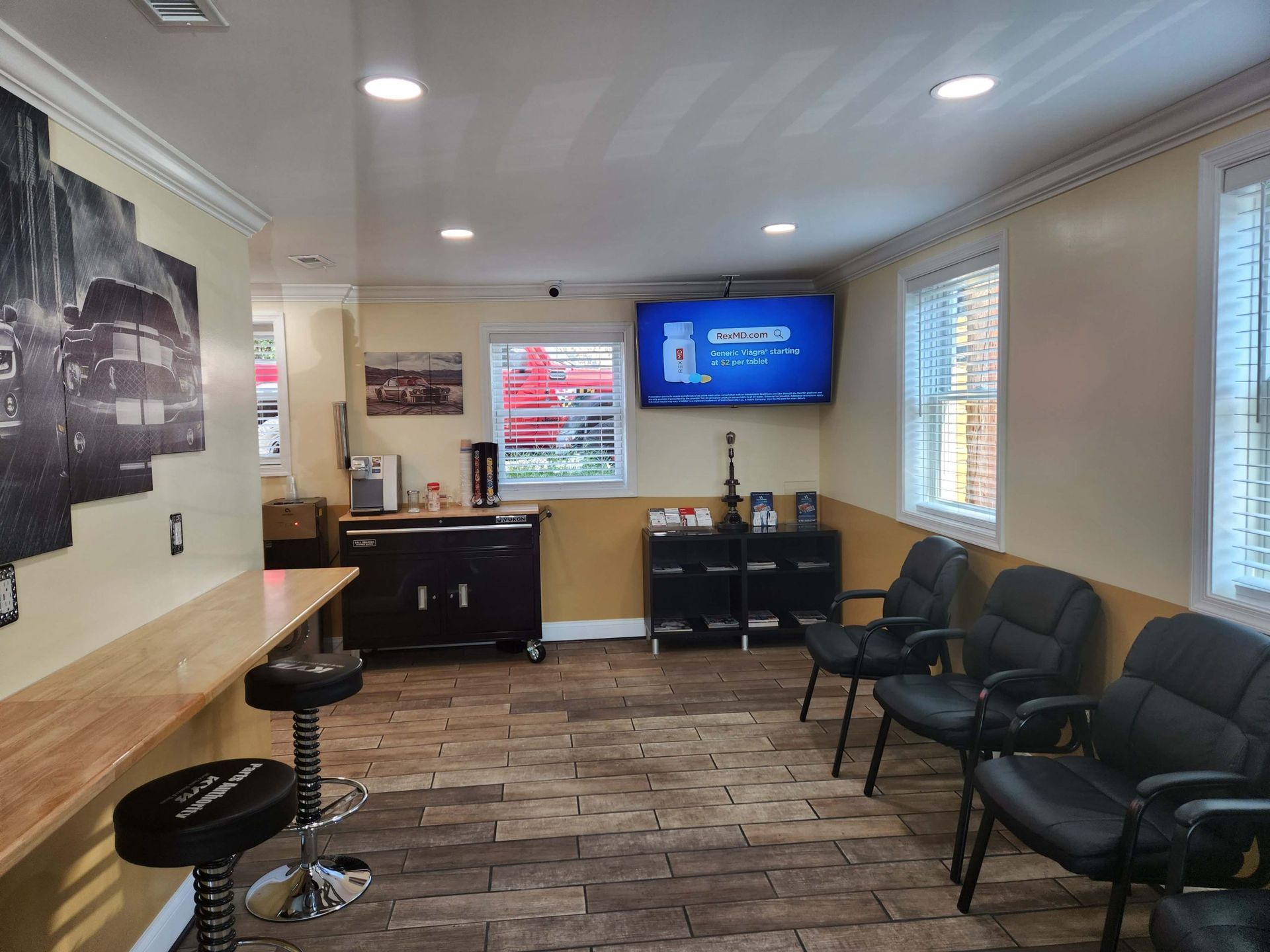 Waiting room with chairs, TV, and counter. Interior features wood-look tile, beige walls, and a window.