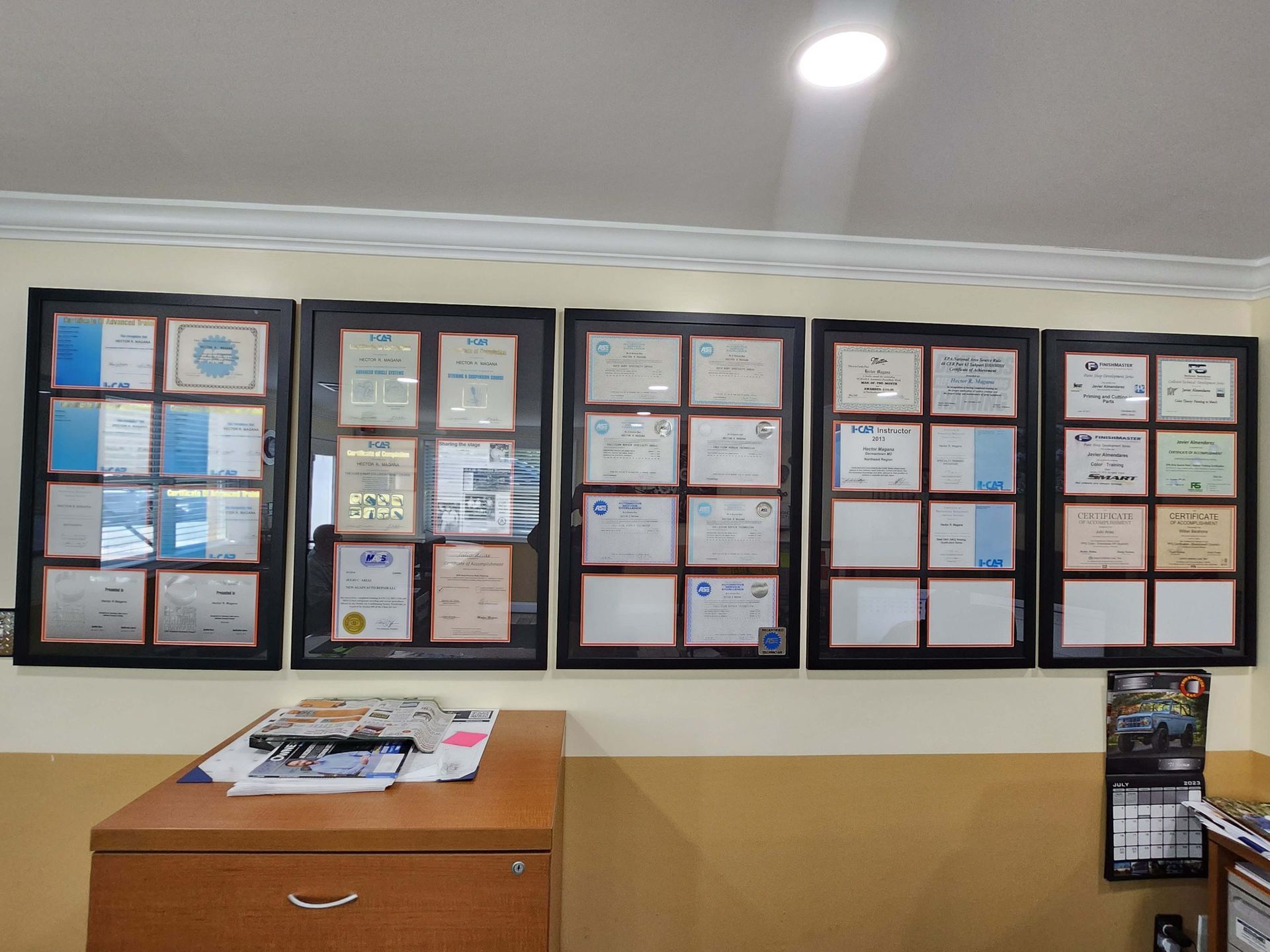 Five framed certificates on wall above a wooden desk.