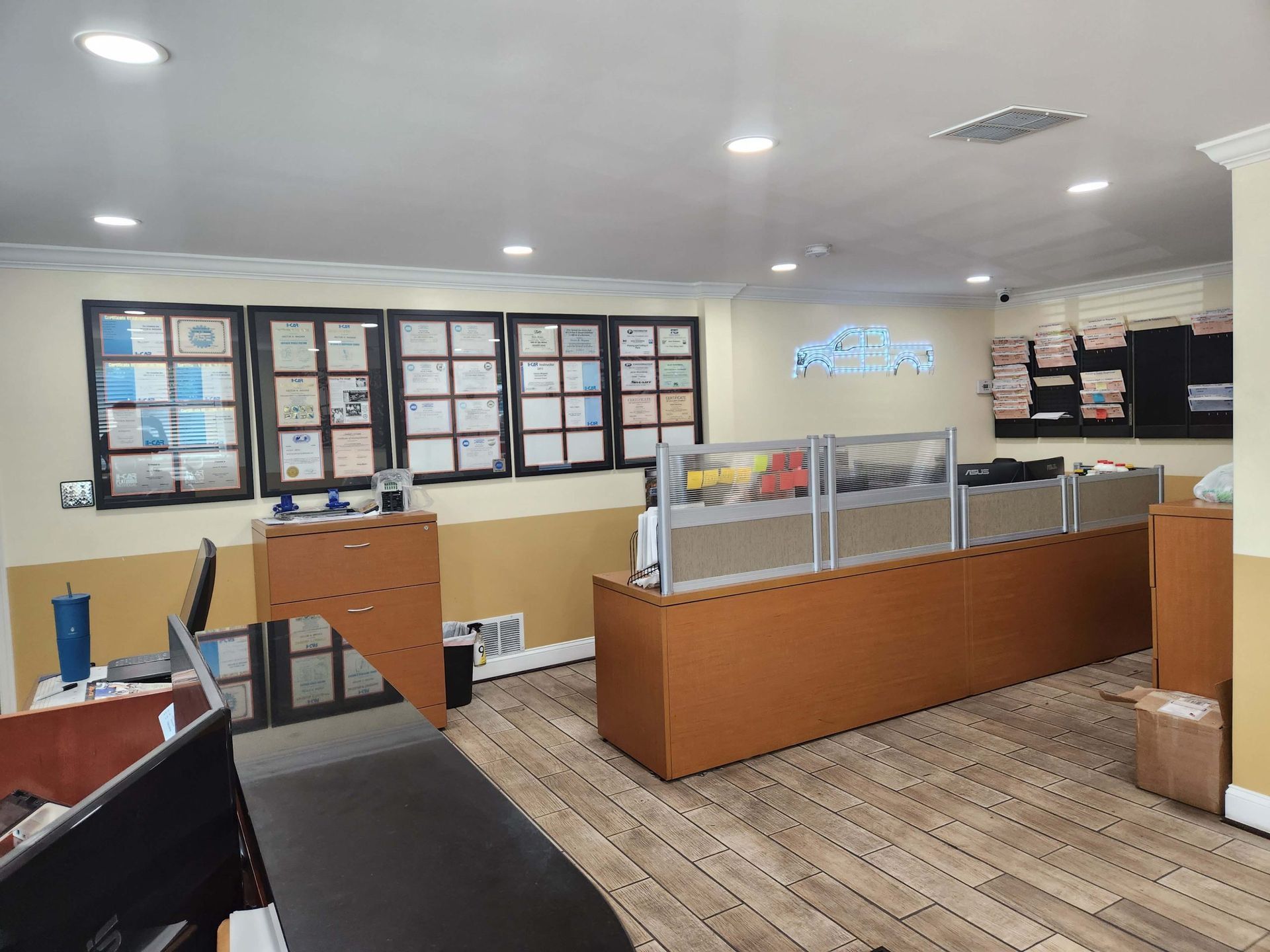 Interior of an office with desks, cubicle dividers, awards on the wall, and documents.