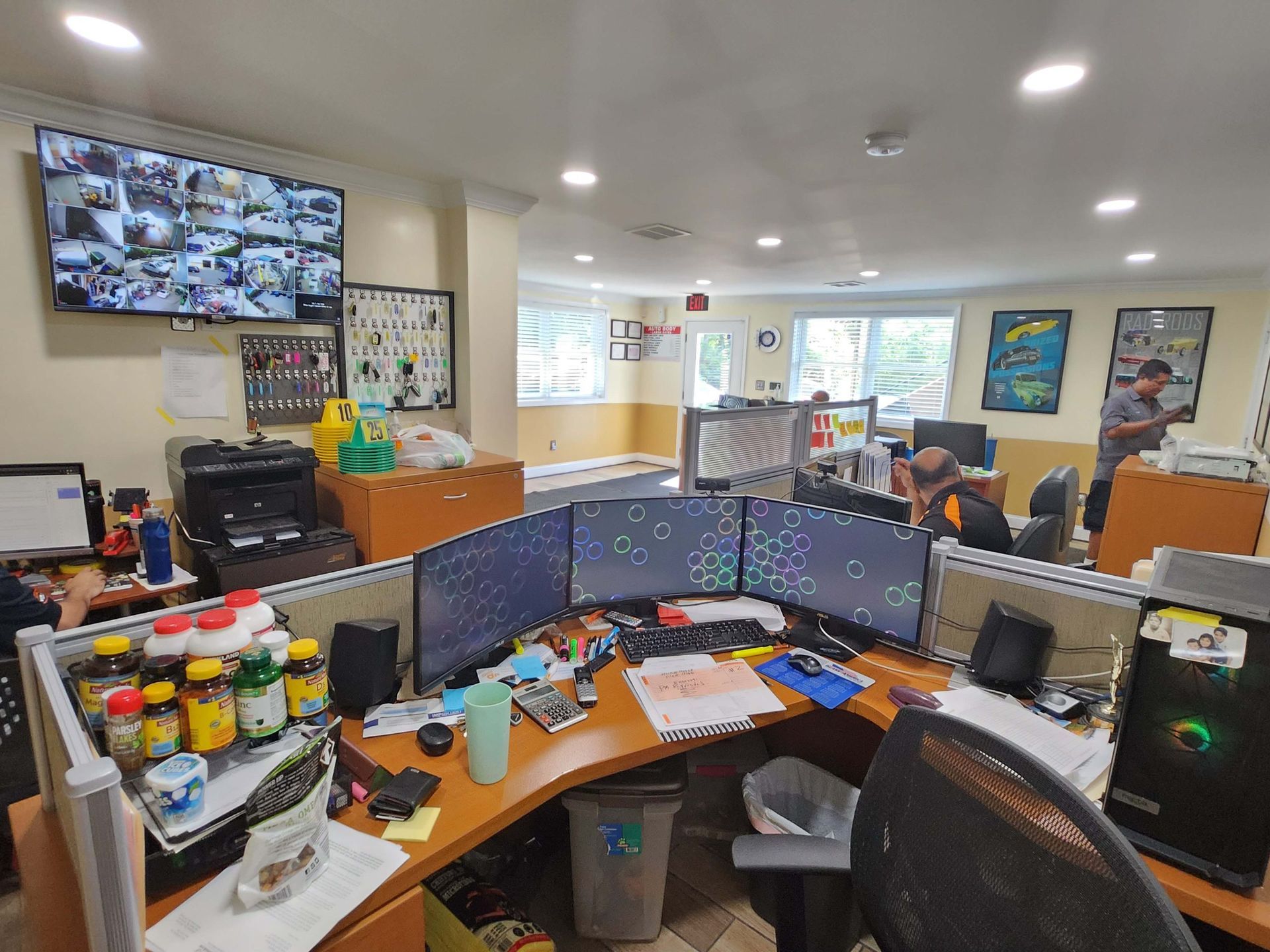 Office interior with computer monitors, security screens, desks, and people working.