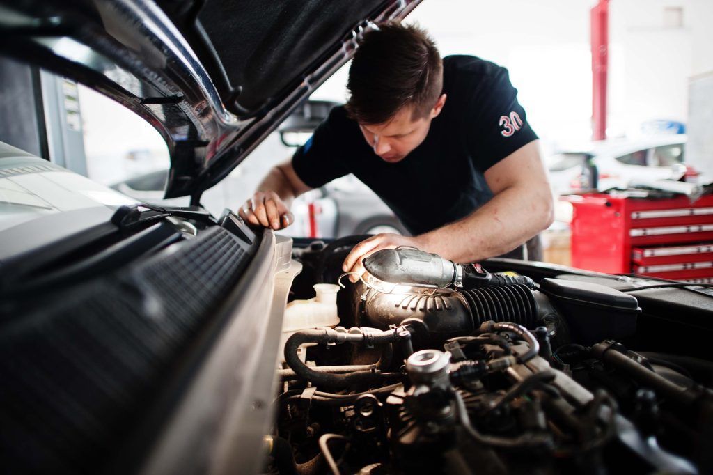 Mechanic working on a car engine in a repair shop.