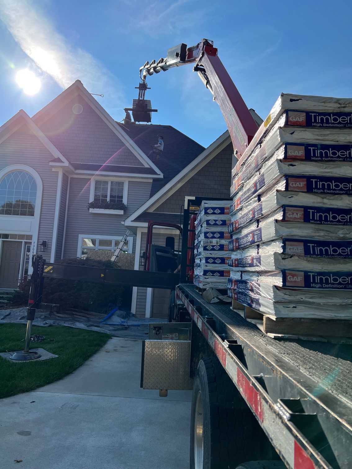 A truck is carrying a stack of timber panels in front of a house.