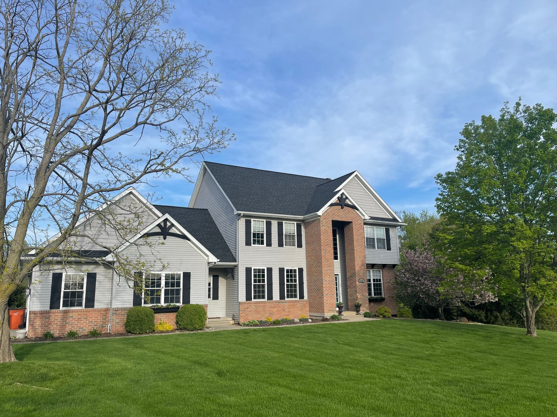 A large white house with a black roof is sitting on top of a lush green lawn.