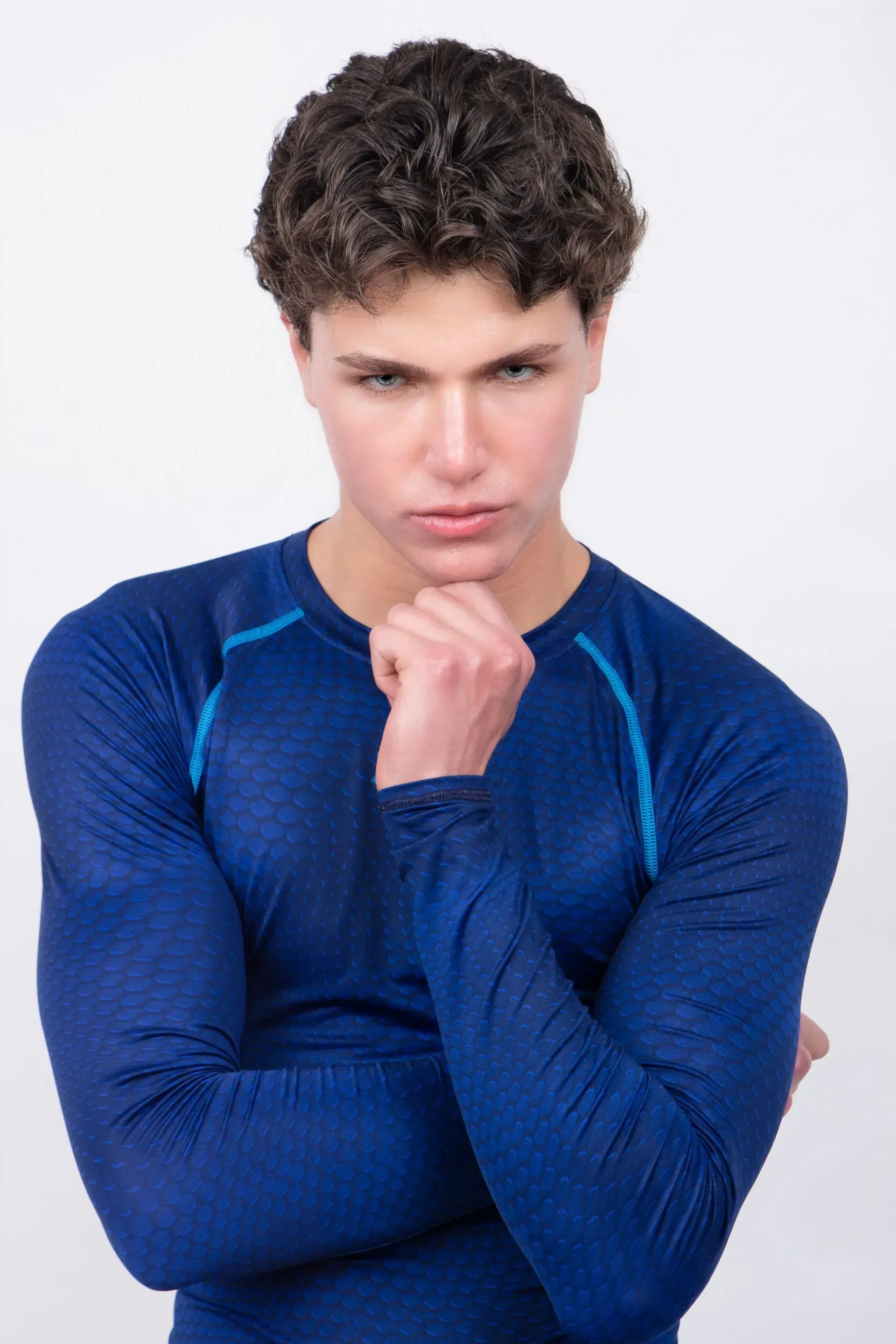 Man in blue athletic shirt, thoughtfully touching chin, looking directly at the viewer.