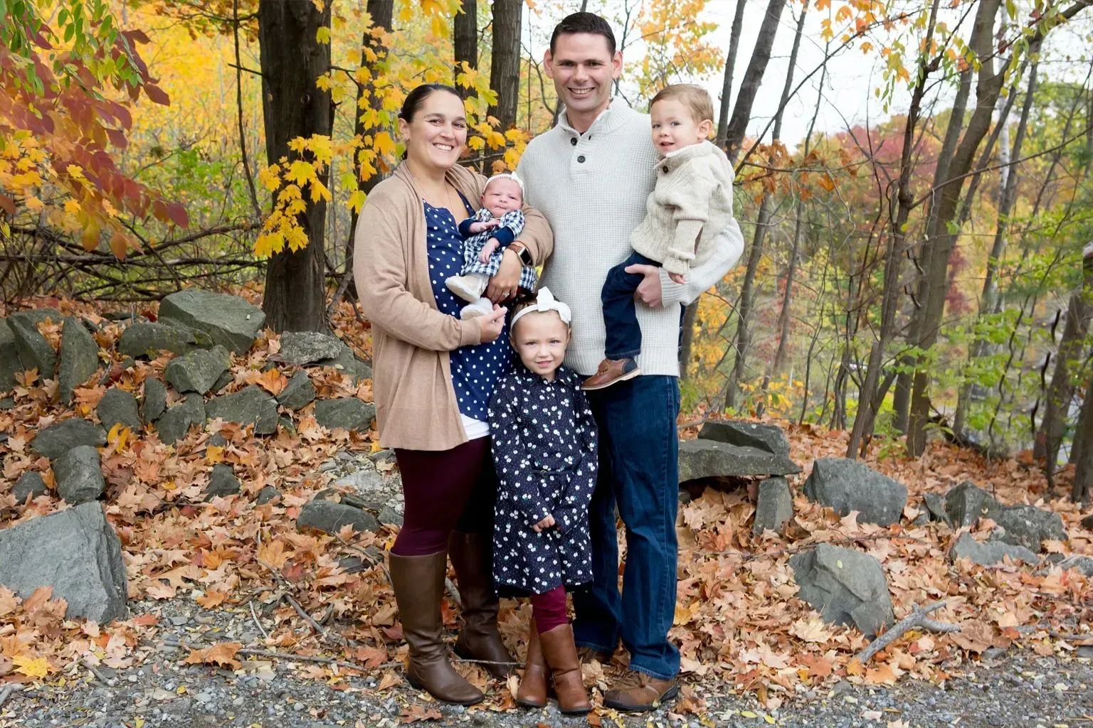 Family of five poses outdoors in autumn, surrounded by colorful foliage.