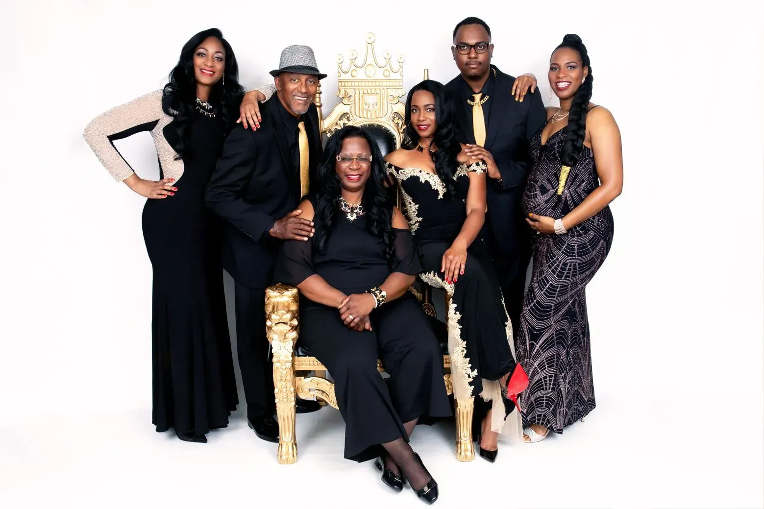 Family of seven poses together, dressed in black and gold attire. Woman seated on ornate gold throne.