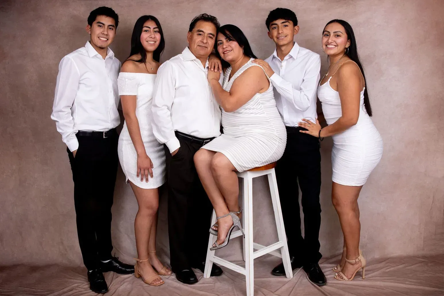 Family of six in white outfits poses in front of a neutral backdrop.