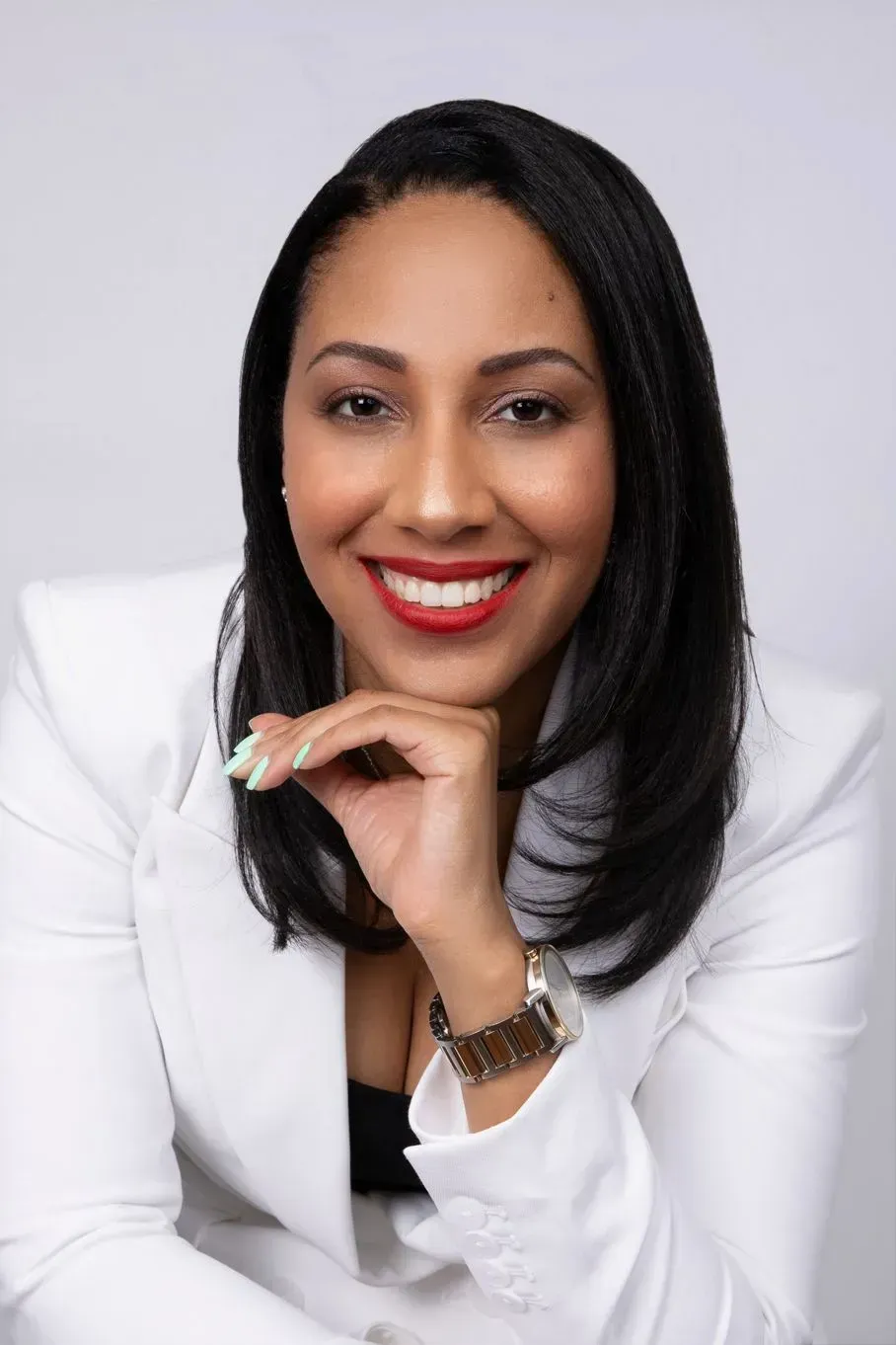 Woman in white blazer smiling, resting chin on hand.