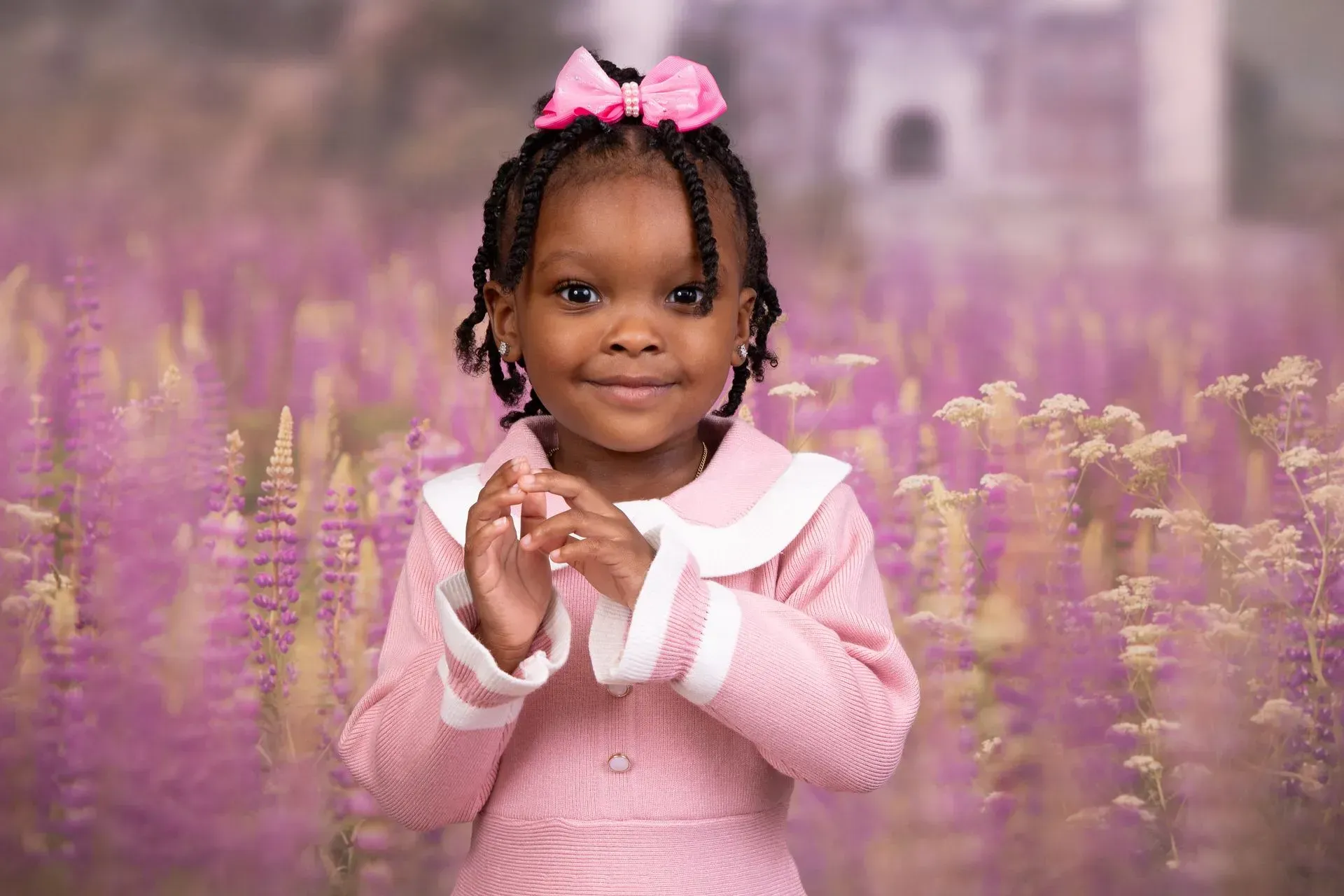 Young girl in pink dress and bow, clapping, in a field of purple flowers.