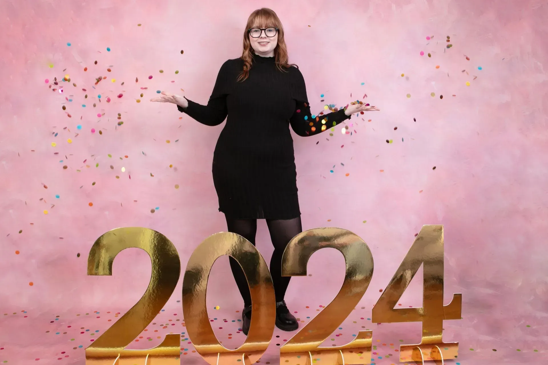 Woman in black dress stands before gold 