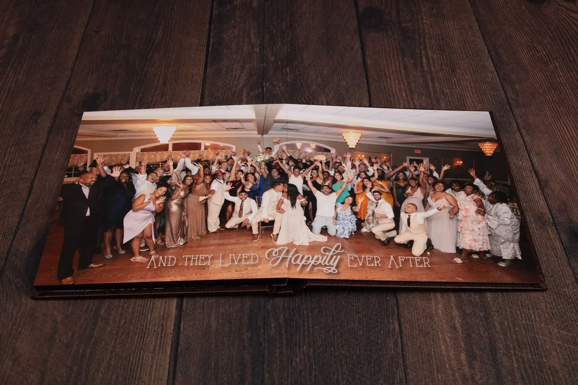 Wedding album opened to a photo of a large group posing and celebrating inside a venue. Text on the album reads 