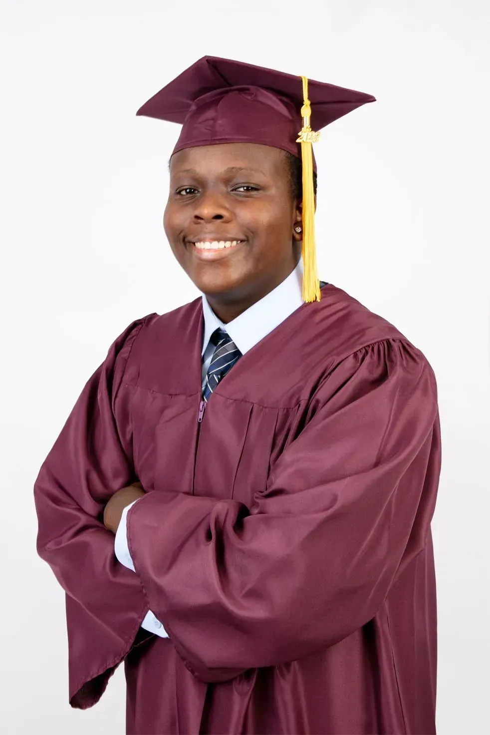 Person in maroon graduation cap and gown, arms crossed, smiling against a white background.