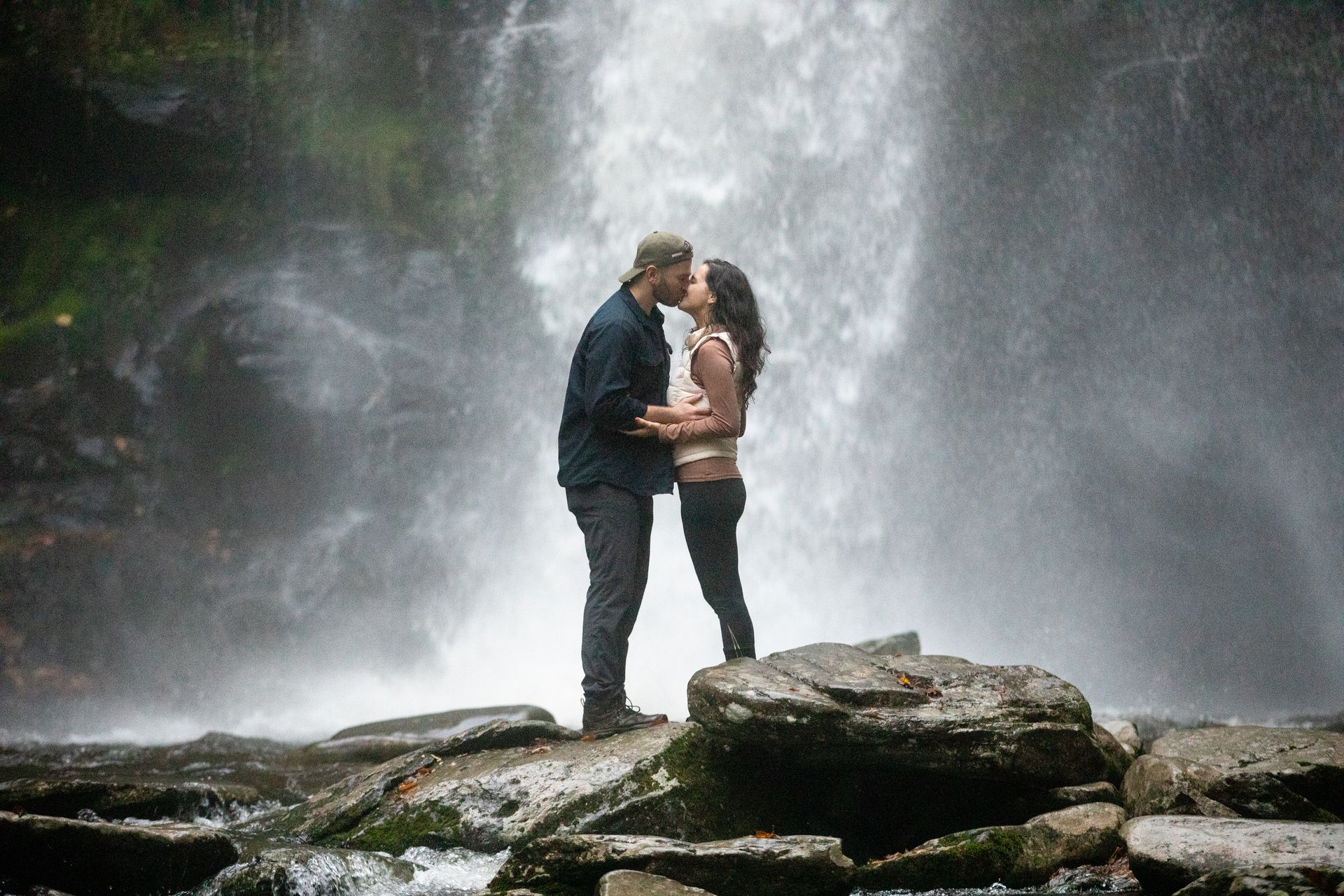Couple kissing on rocks before a misty waterfall