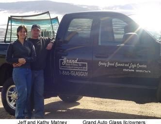 Two people standing beside a black pickup truck with business decals in a sunny outdoor lot