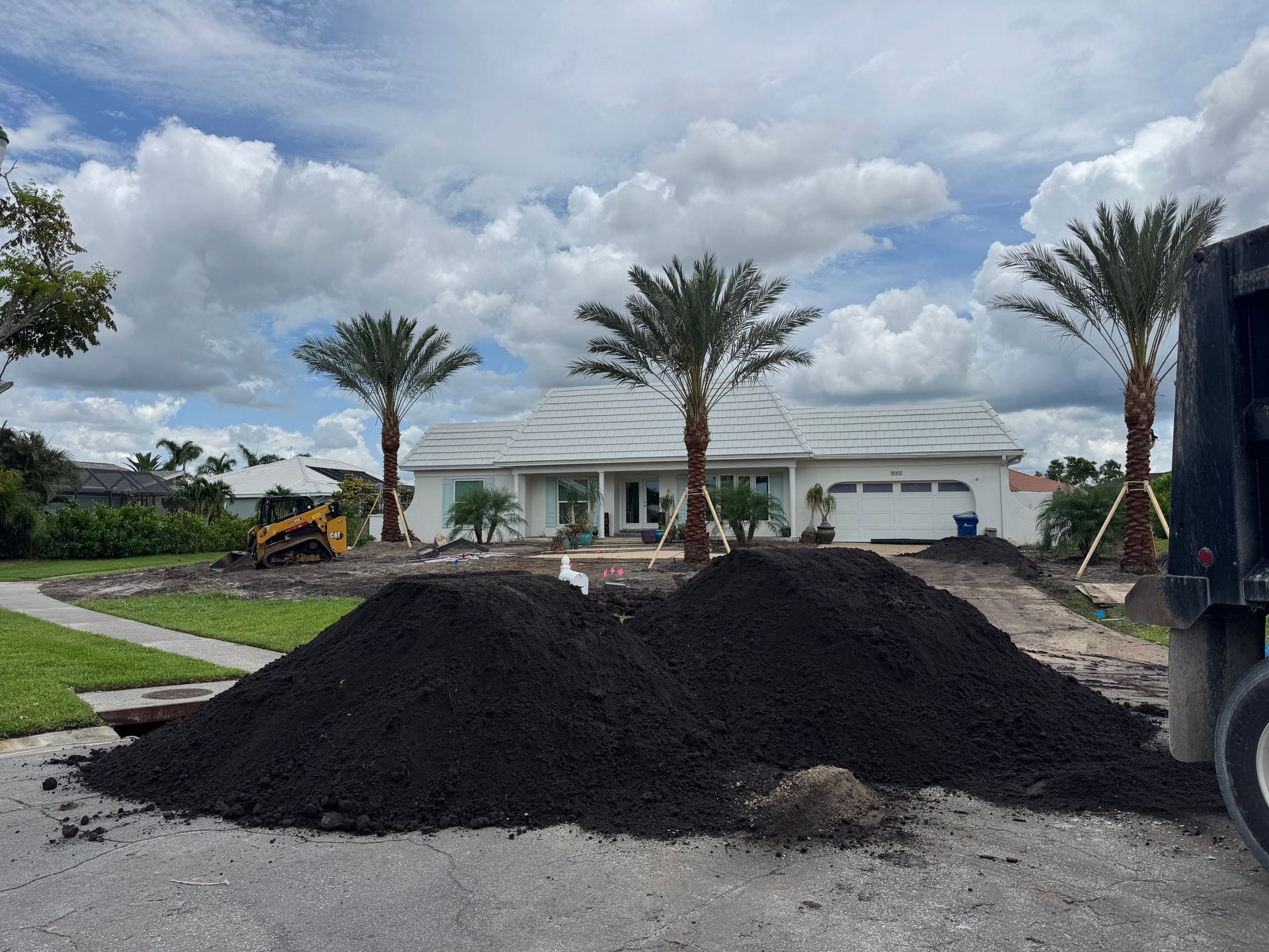 A pile of dirt is in front of a house with palm trees.