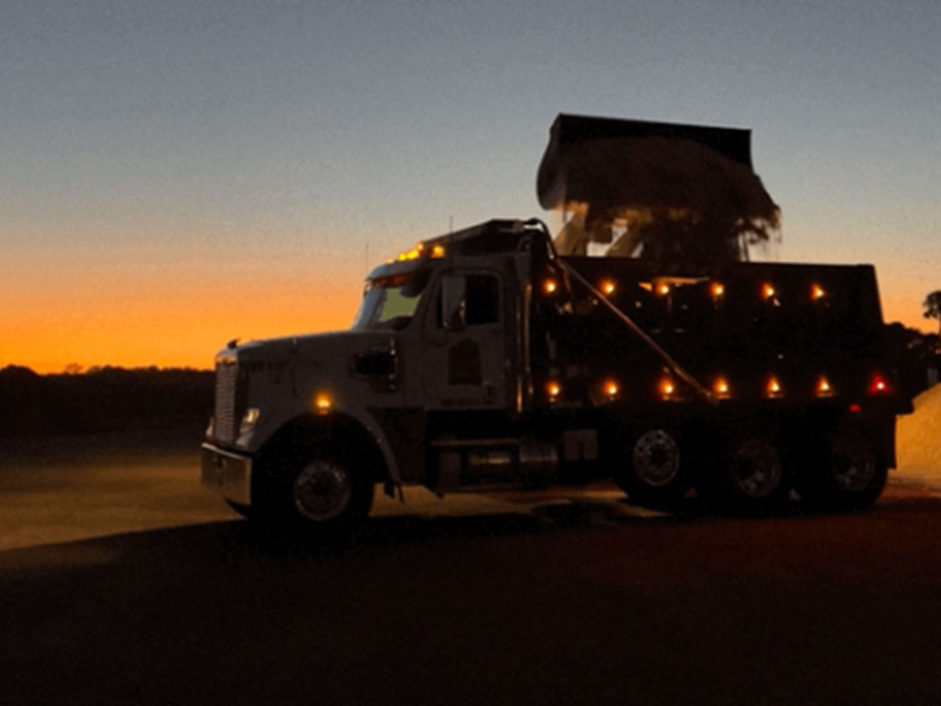 A dump truck is parked on the side of the road at sunset