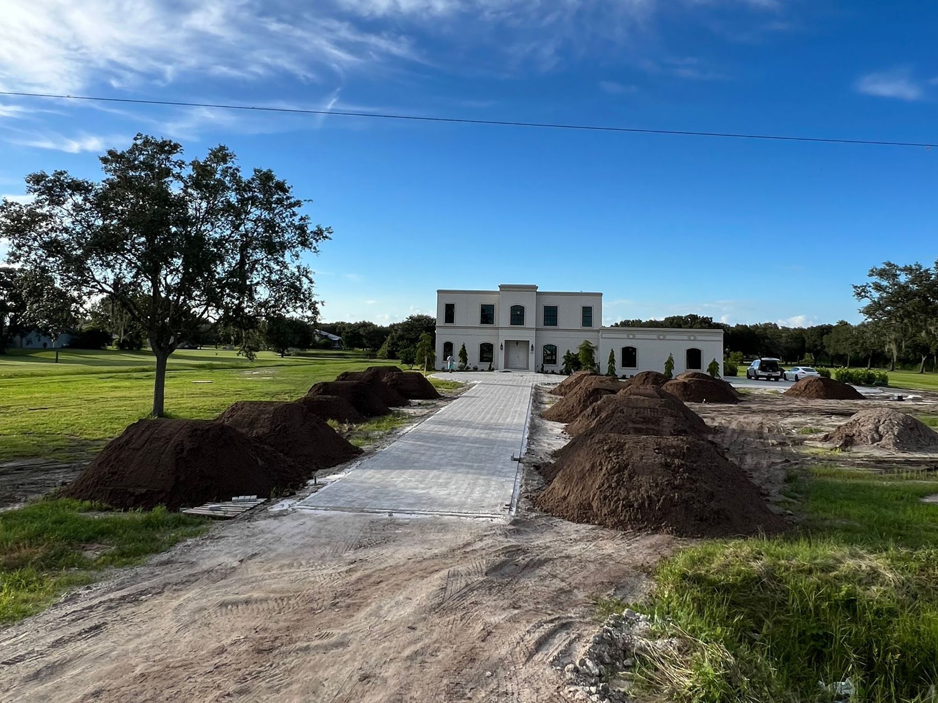 A dirt road leading to a large house with piles of dirt in front of it.