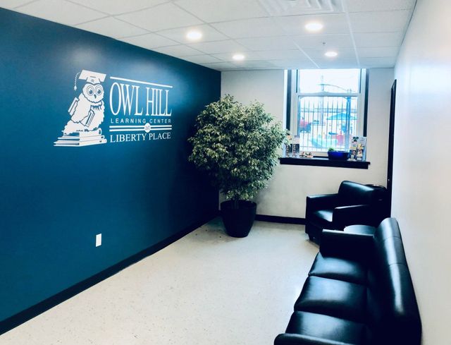 Modern office waiting area with teal wall logo, black chairs, potted plant, and window light