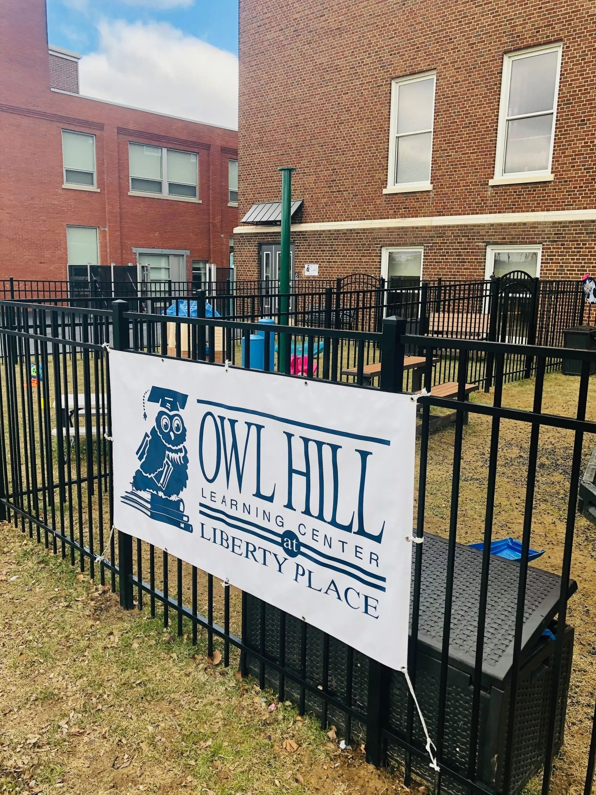 Owl Hill Liberty Place sign on a black fence in front of brick apartment buildings.