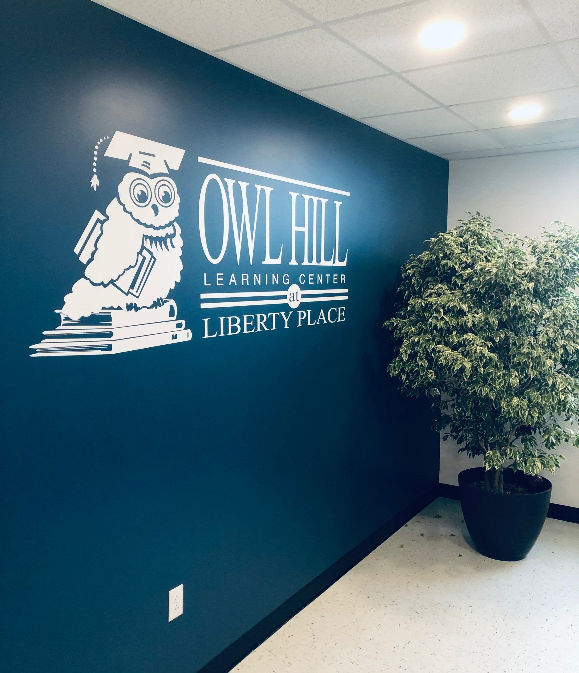 Quill Hill Farmington Library sign on teal wall beside a potted tree in a hallway