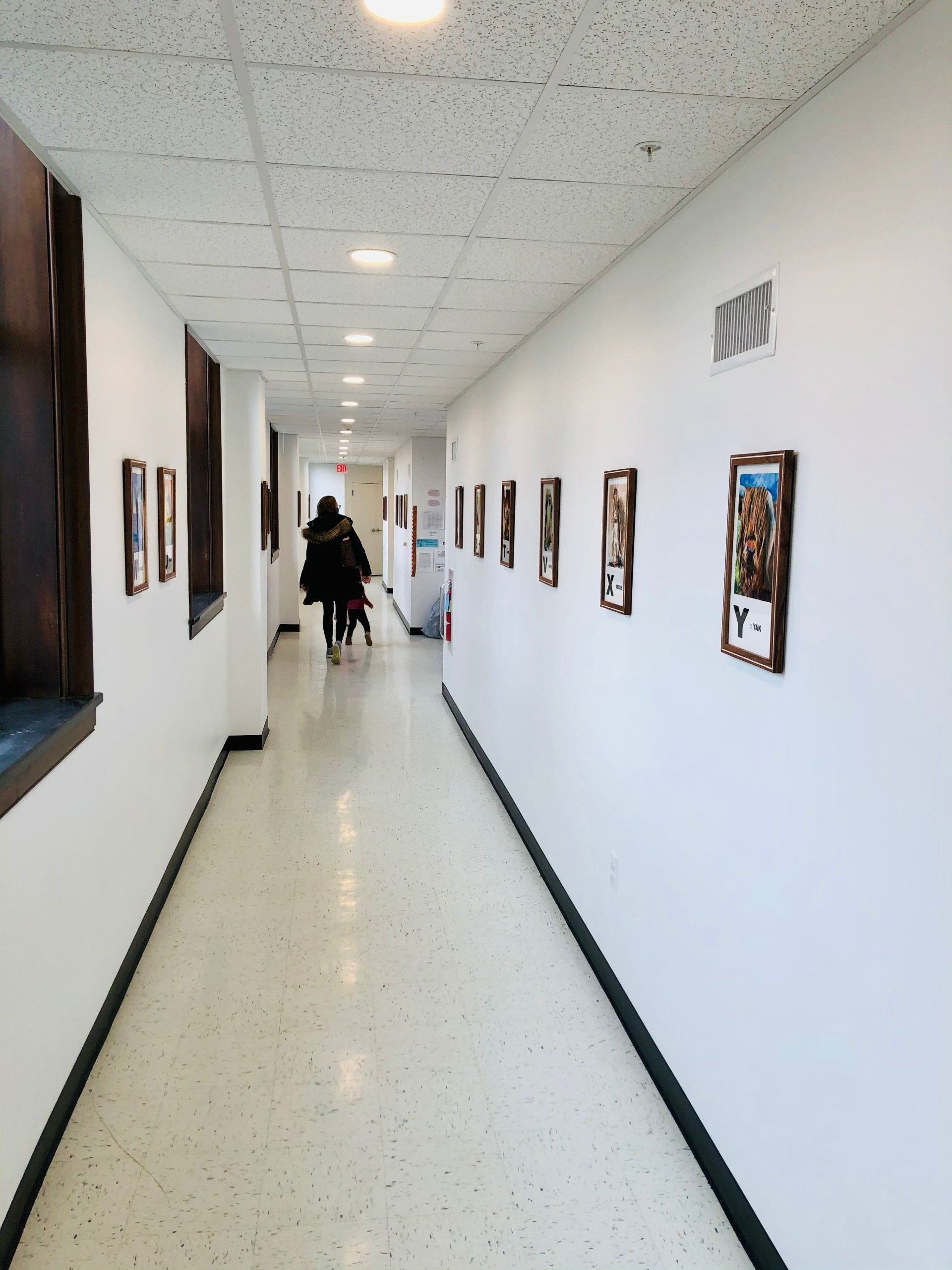 Bright hallway with framed wall art and a person walking away near the far end