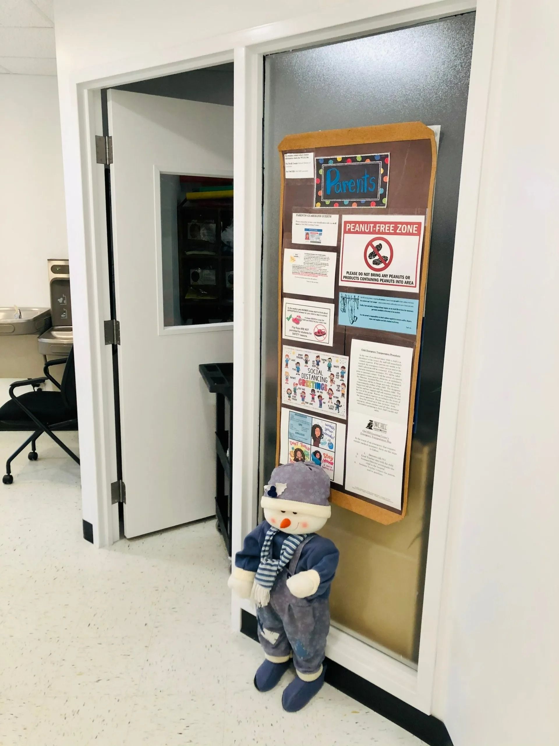 Open office doorway with a bulletin board covered in notes and a stuffed snowman by the door