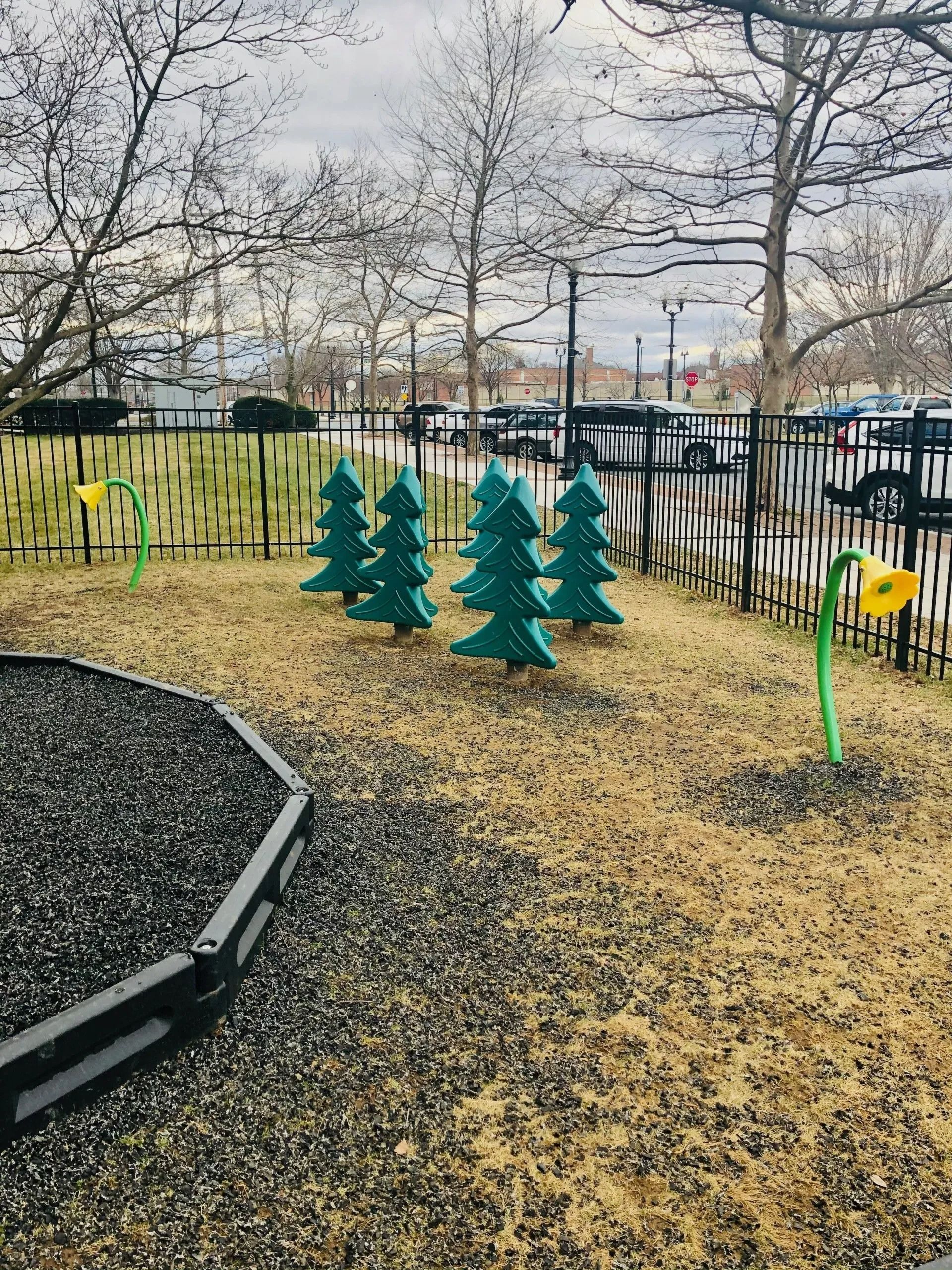 Small fenced playground with colorful tree decorations and yellow flowers on a cloudy day