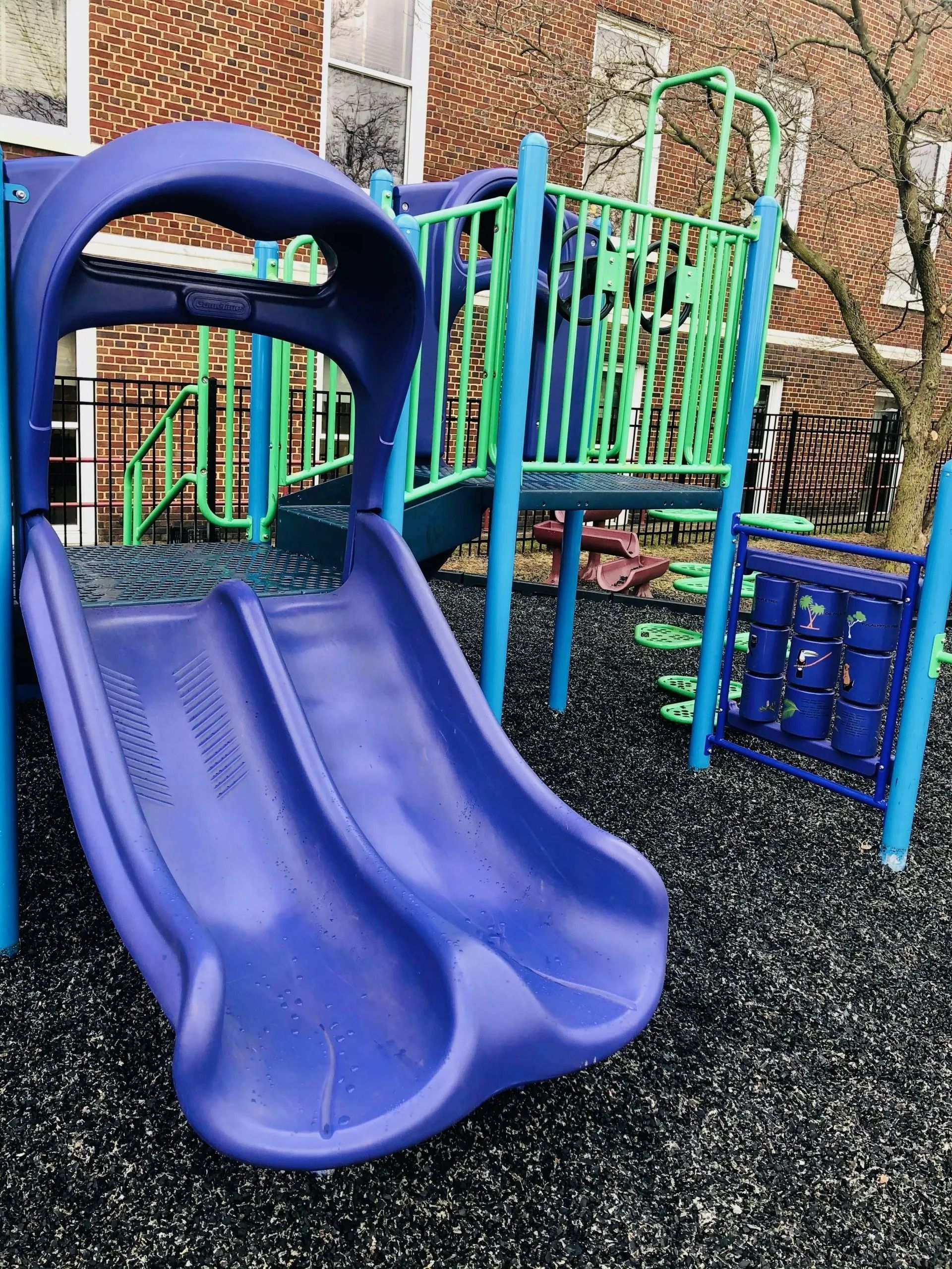 Blue double slide on a colorful playground with climbing structures and rubber safety flooring