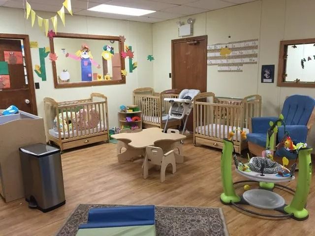 Childcare playroom with cribs, toys, and rocking chairs in a cozy indoor space
