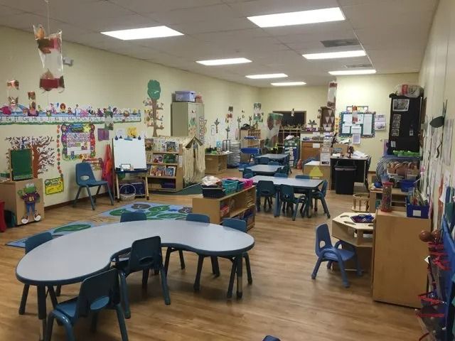 Colorful preschool classroom with tables, chairs, toys, and learning materials on the walls