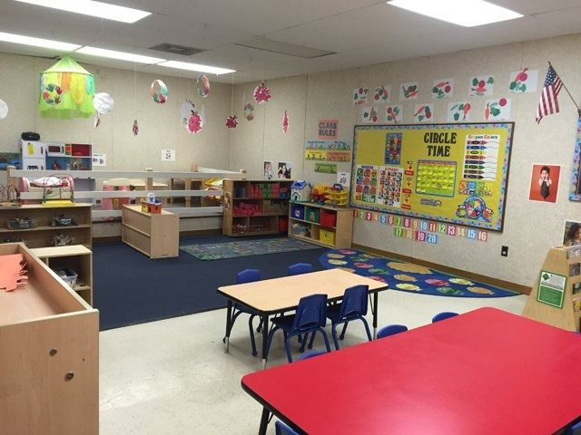 Colorful preschool classroom with tables, shelves, rugs, and bulletin boards.