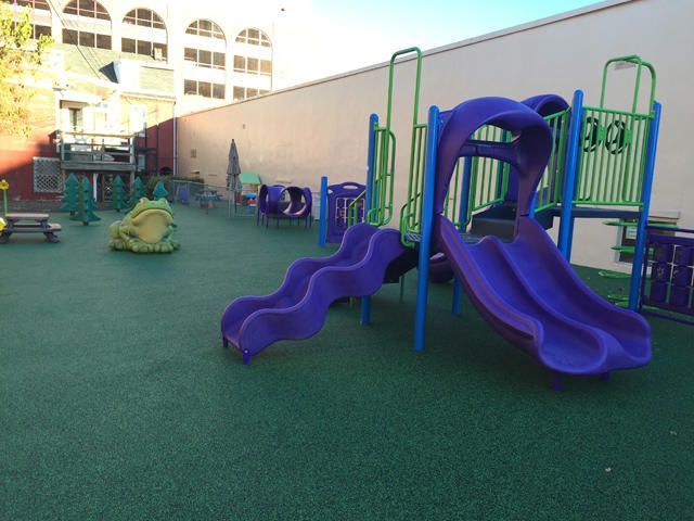 Outdoor playground with purple slides and green climbing structures on a rubber play surface
