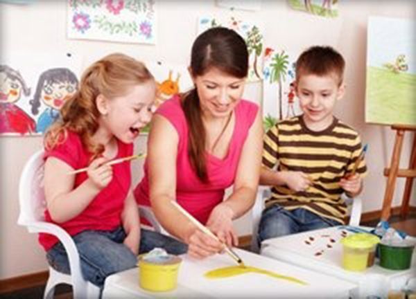 Children and a teacher painting together at a table in a colorful classroom