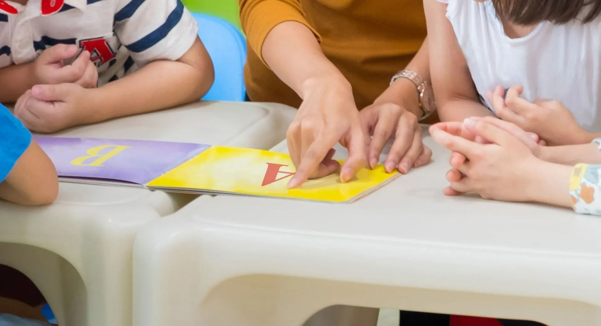 Hands pointing at a colorful worksheet on a white table during a group activity