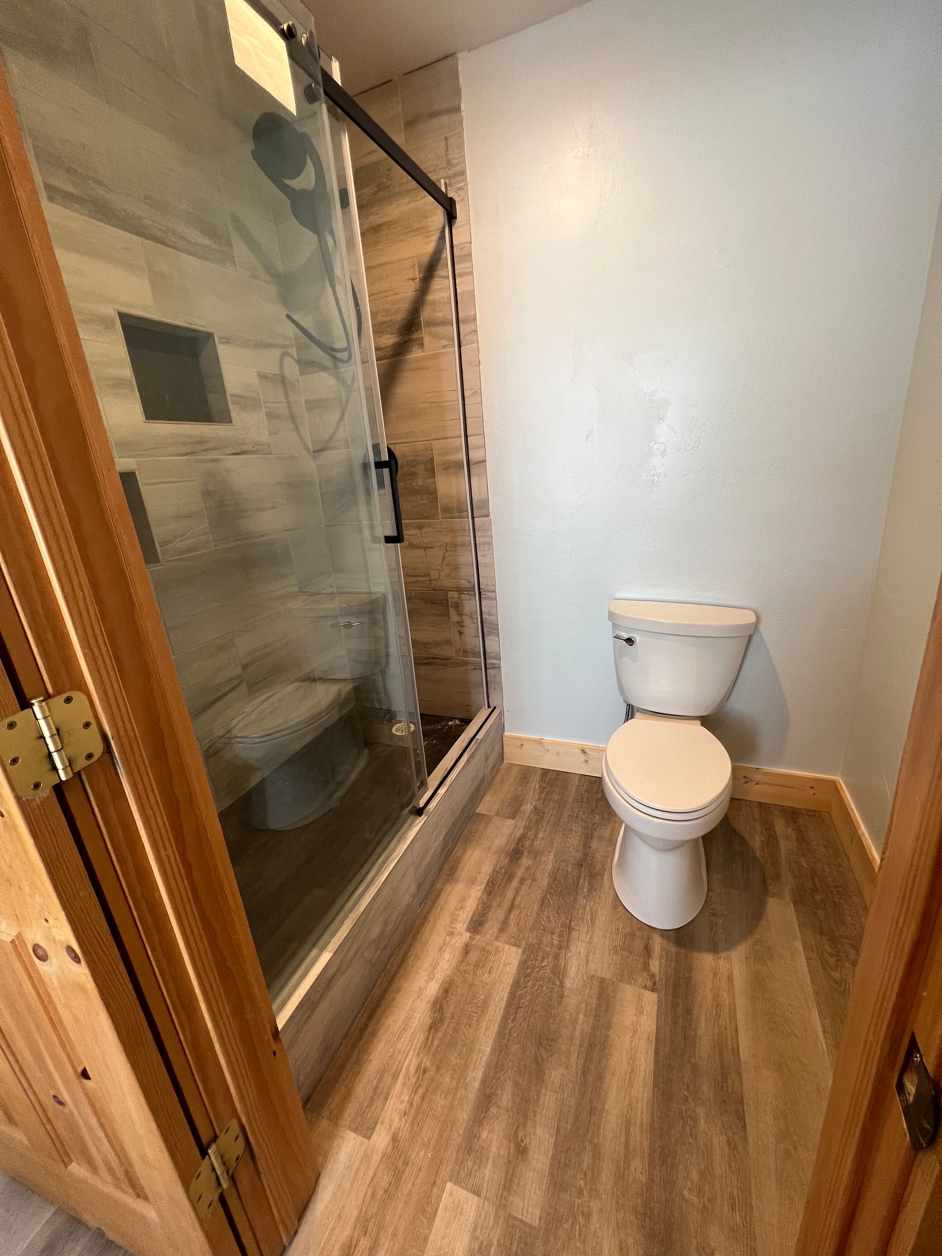 Small bathroom with wooden floor, white toilet, and glass shower enclosure on the left.