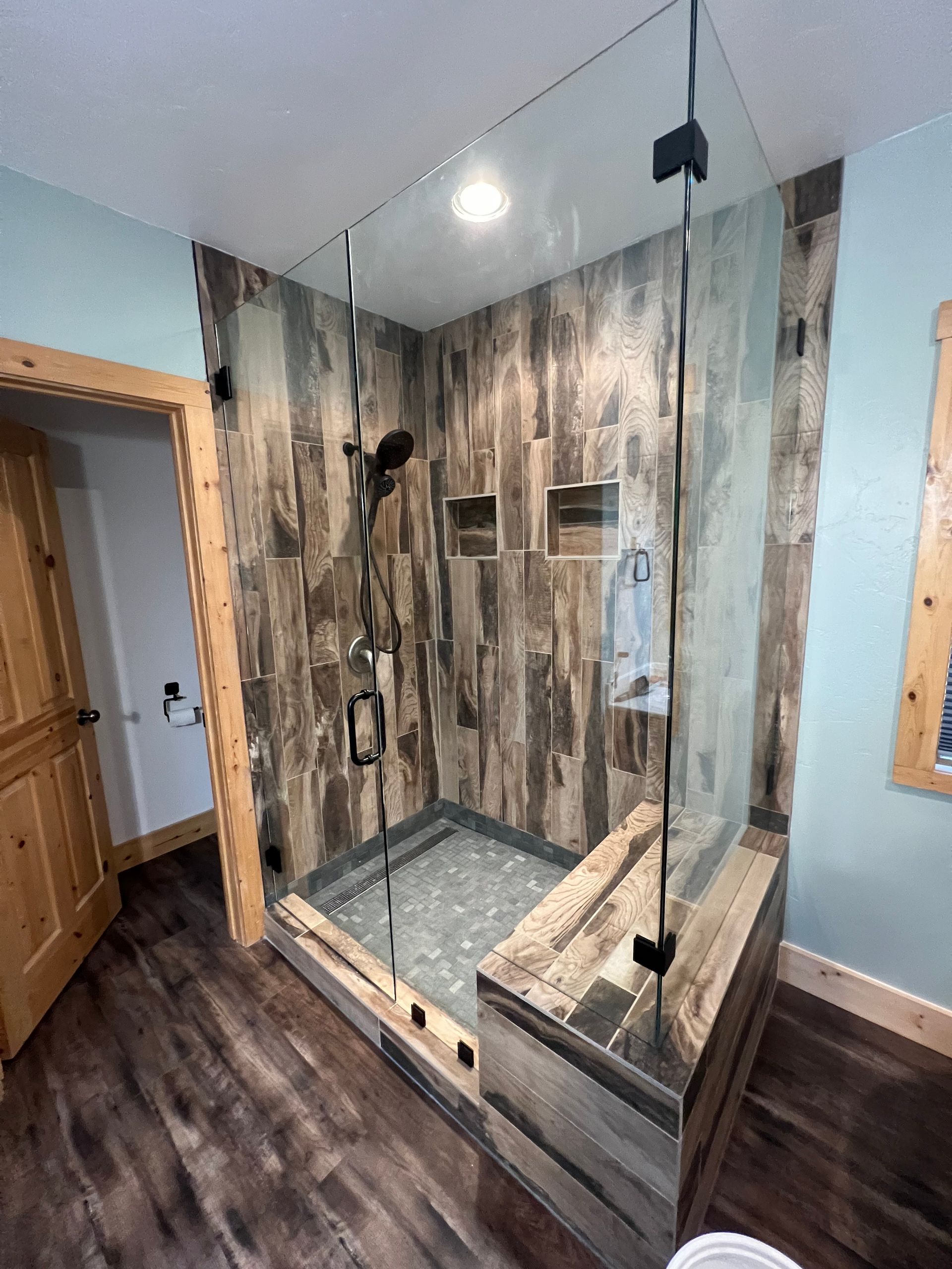 Modern bathroom with glass shower enclosure, wood-look floor, and gray stone tile walls