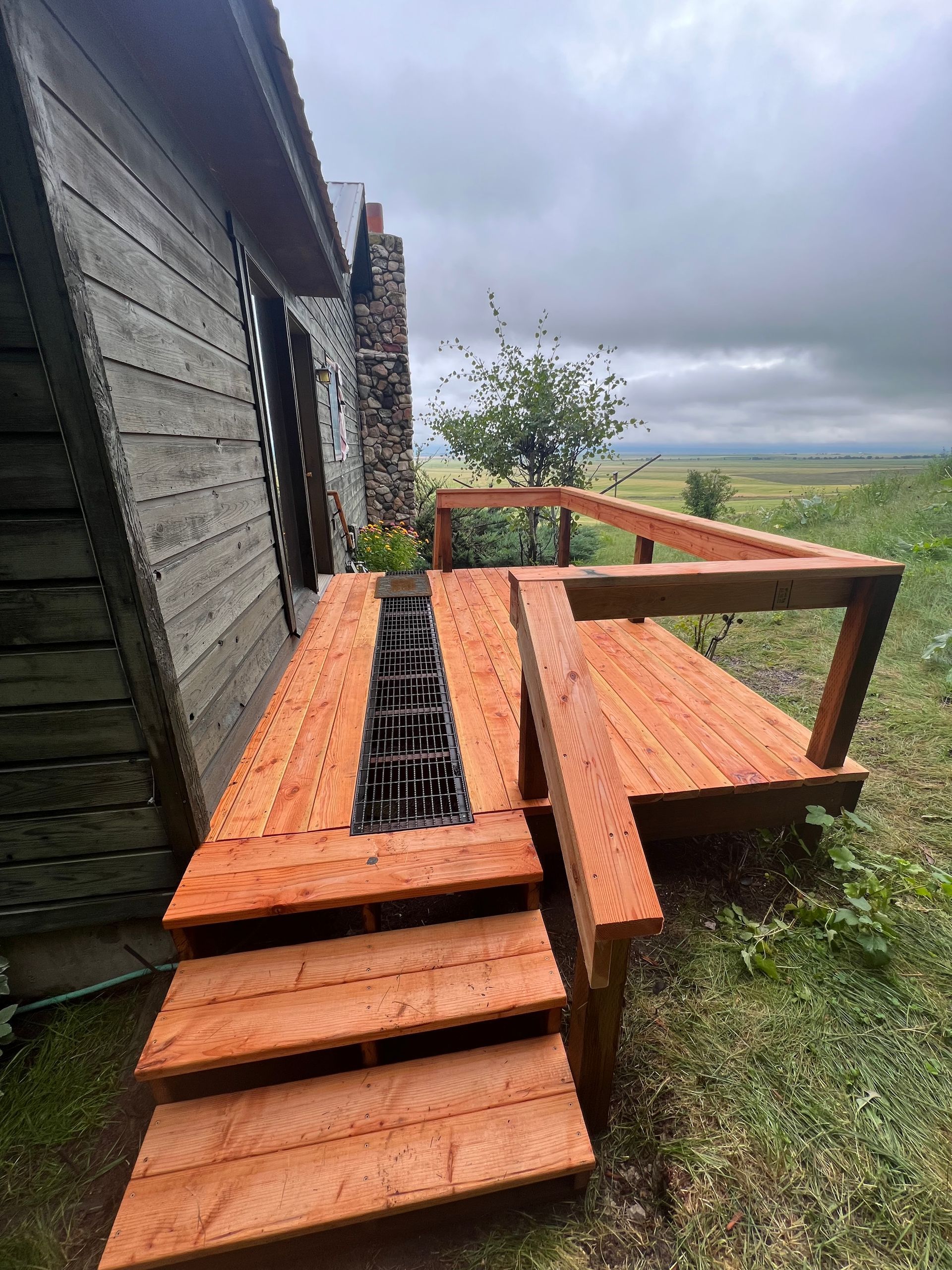 Stacked orange wooden deck boards beside a house under cloudy skies.