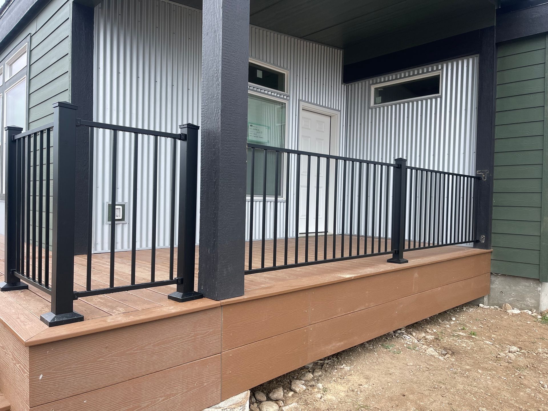 Wooden deck stairs with a railing beside a house, overlooking a grassy landscape under cloudy skies.