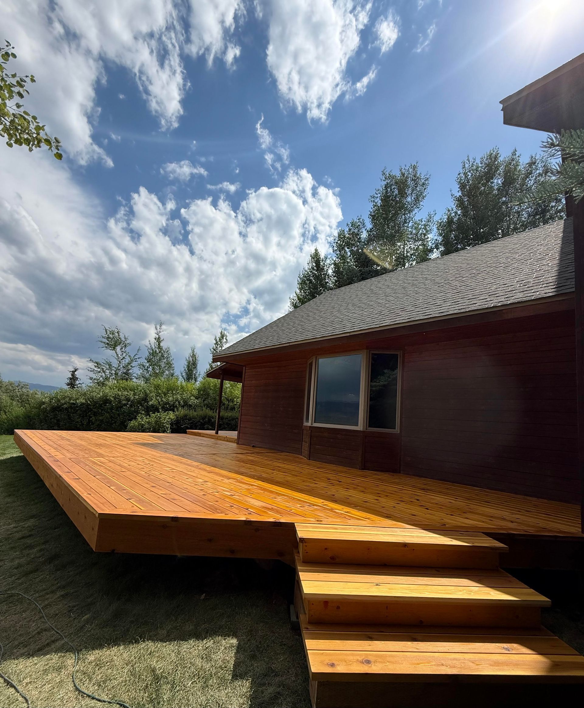 Wooden deck and steps beside a small red cabin under a bright, cloudy sky