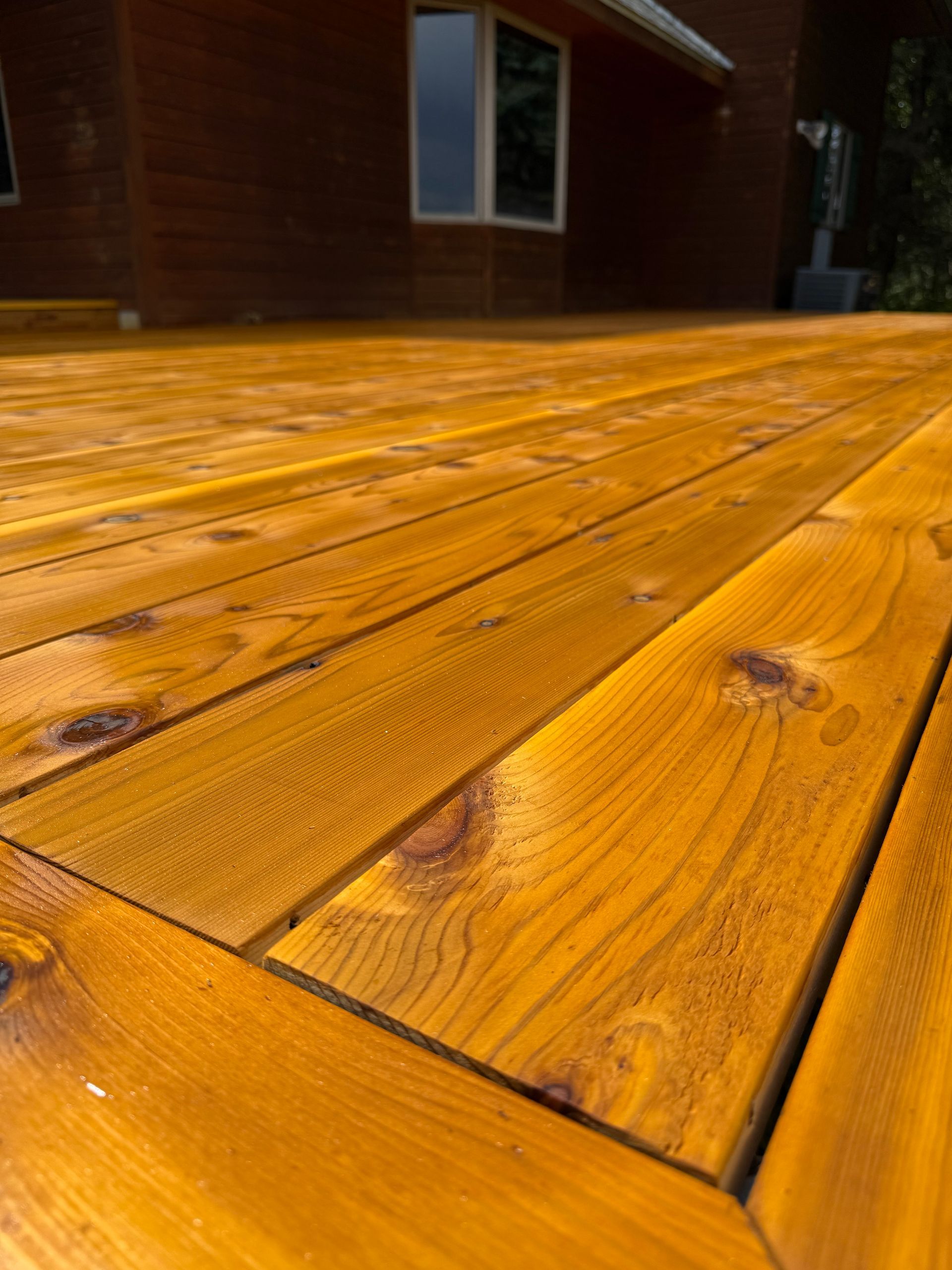 Close-up of a stained wooden deck with visible plank seams beside a house exterior