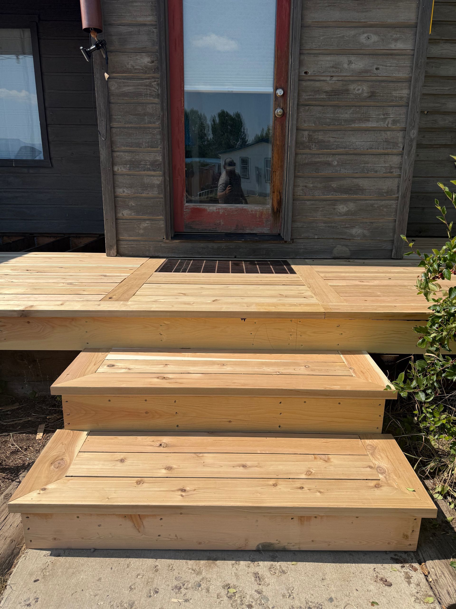 Wooden steps leading to a deck and glass door on a rustic cabin exterior.