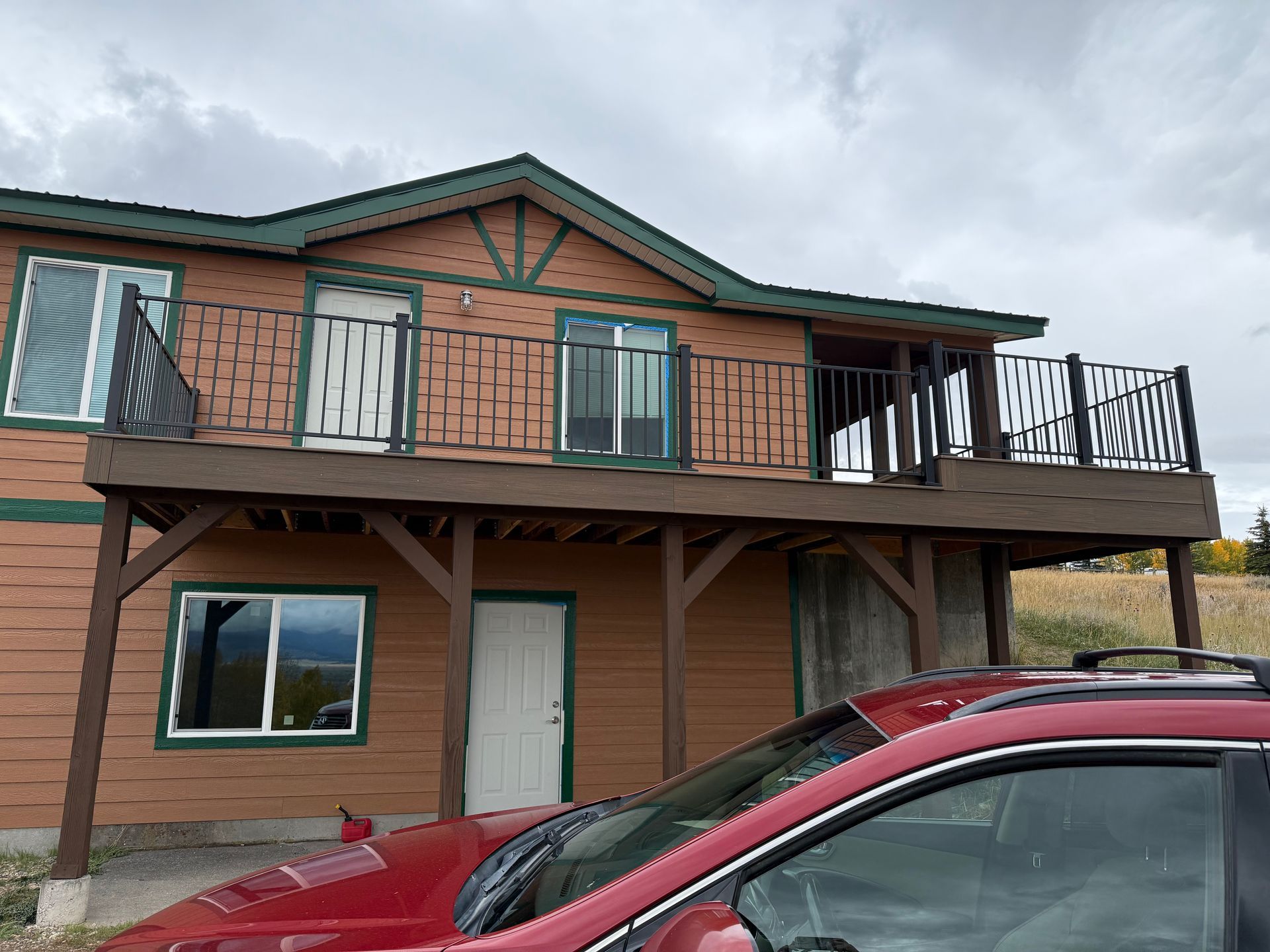 Two-story brick house with a wooden balcony and red car parked in front under cloudy skies