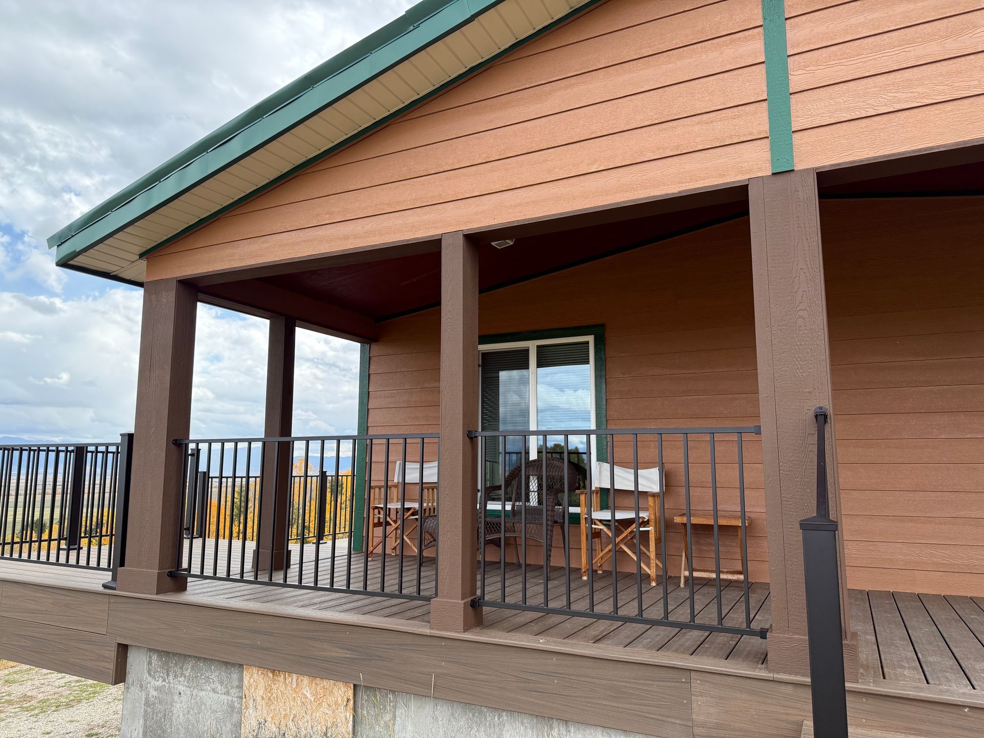 Wooden porch with railing on a cabin-like house, featuring a covered deck and outdoor seating.