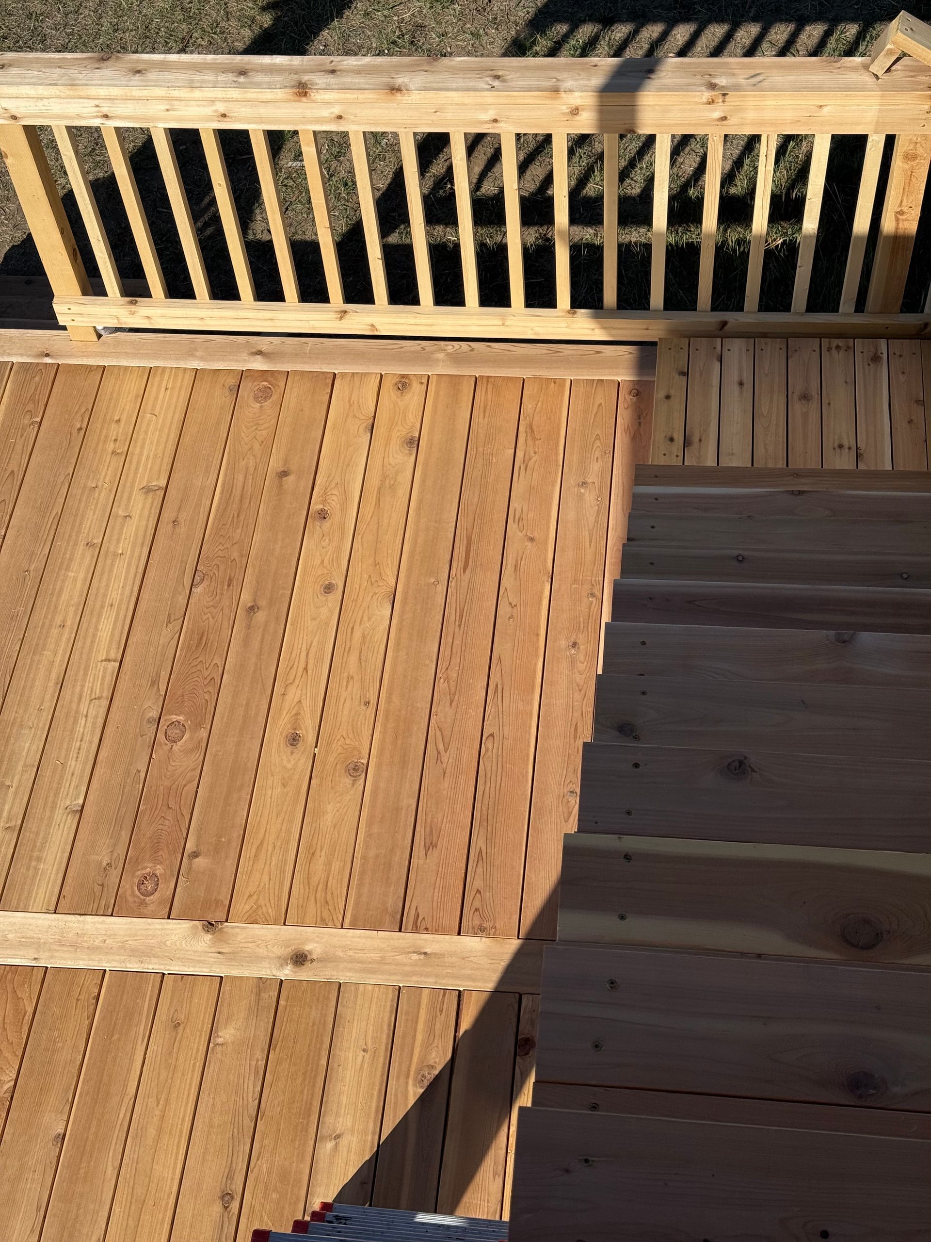 Wooden deck with sunlit railing and a shadow across the floorboards.
