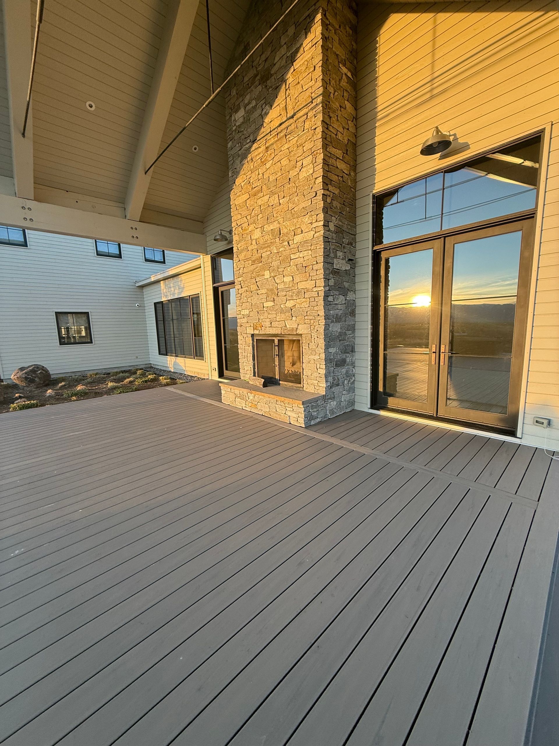 Covered patio with gray deck, stone column, and sliding glass doors at sunset