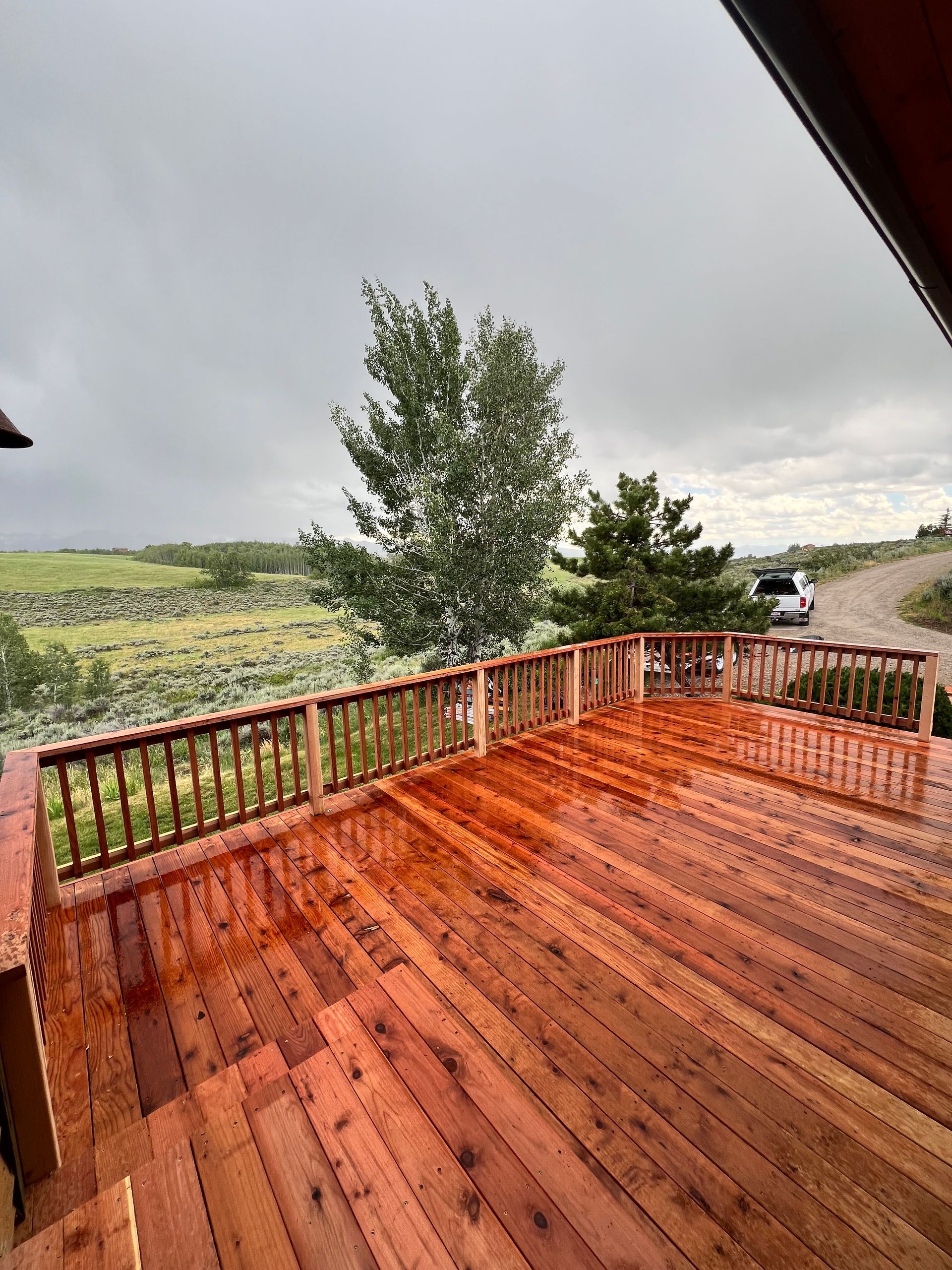 Wet wooden deck overlooking a cloudy rural field and a parked car