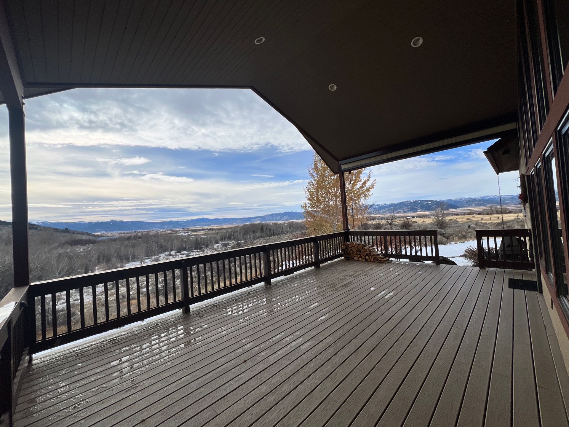 Covered wooden deck overlooking snowy mountains and cloudy sky
