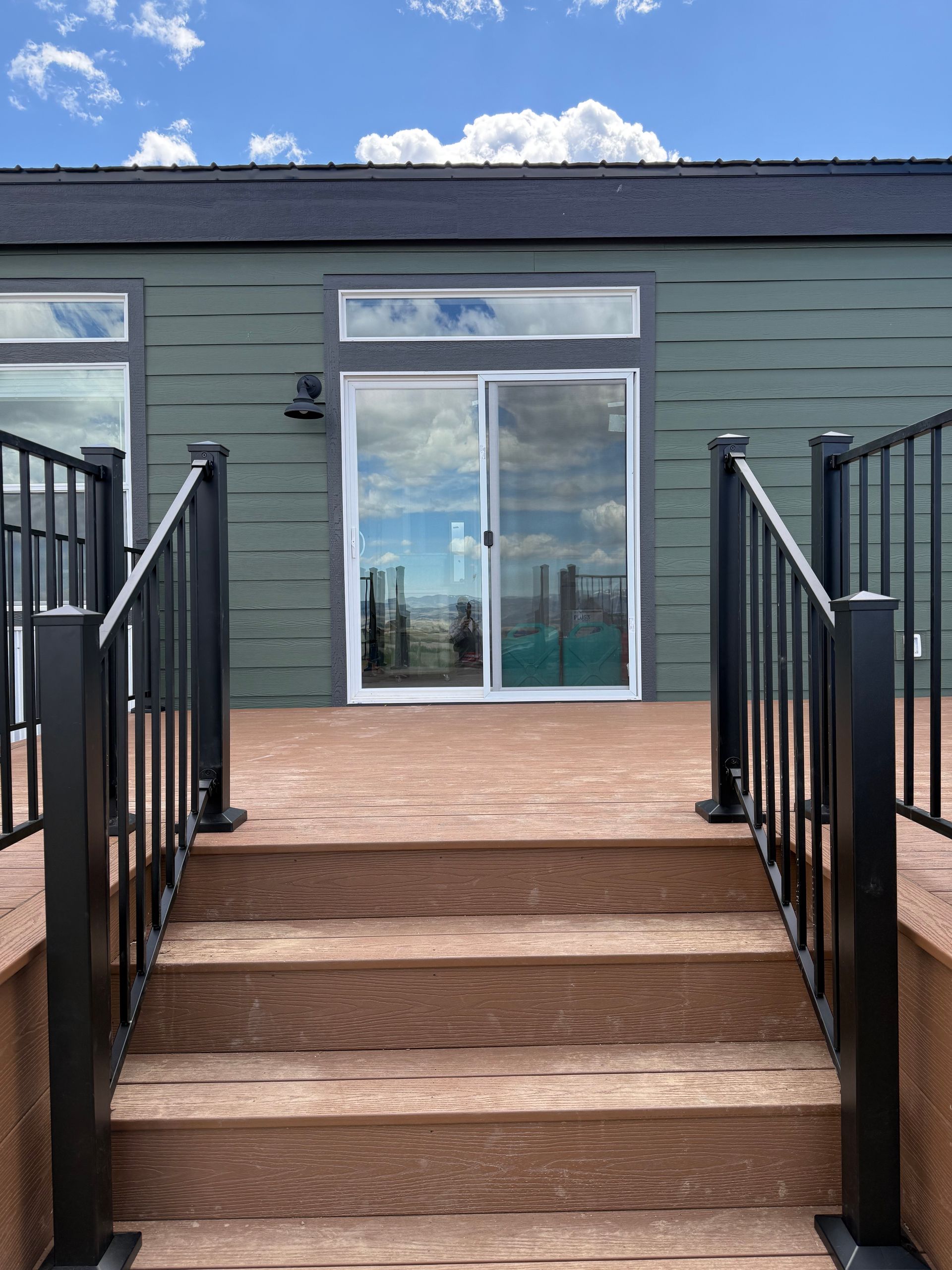 Outdoor stairs leading to a terrace with black railings and a green wall with a glass door